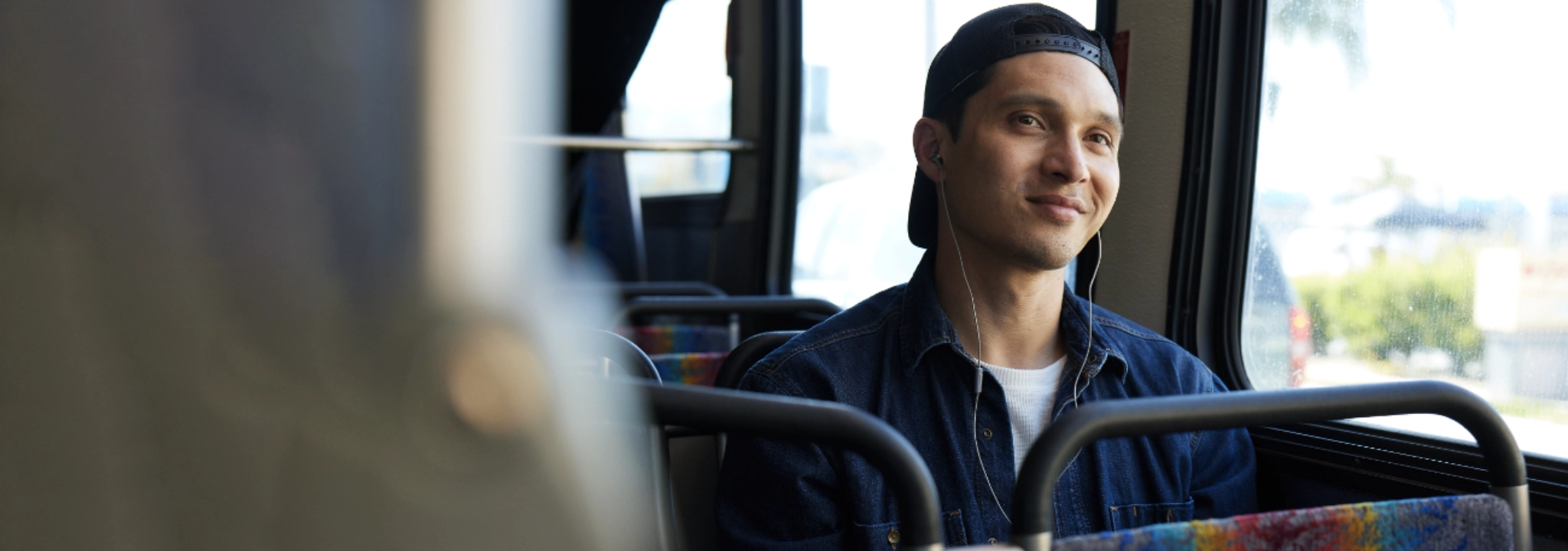 Medium distance shot of a man sitting on a bus listening to music and smiling